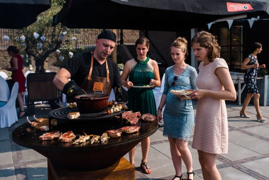 Grillmeester grilt vlees op een ronde houtgestookte grill tijdens een buitenfeest