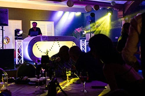 DJ achter de draaitafel met feestverlichting en gasten aan tafel bij De Haas