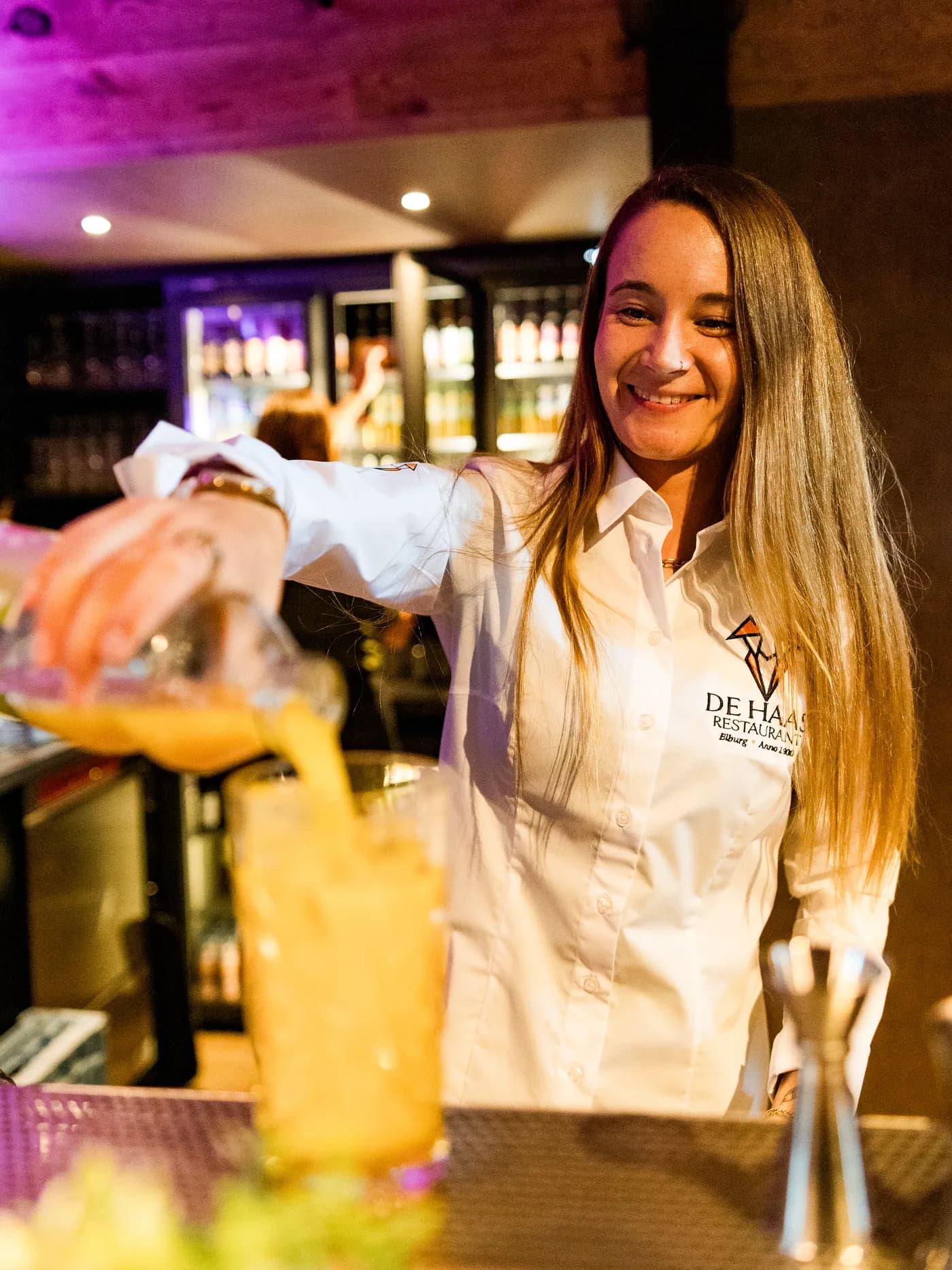 Lachende medewerker van De Haas schenkt een cocktail in aan de bar