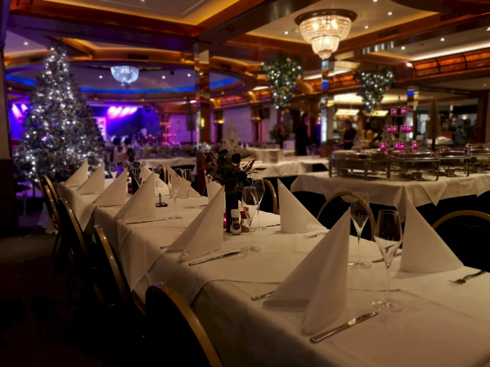 Feestelijk gedekte lange tafels met witte servetten en een kerstboom in de feestzaal van De Haas