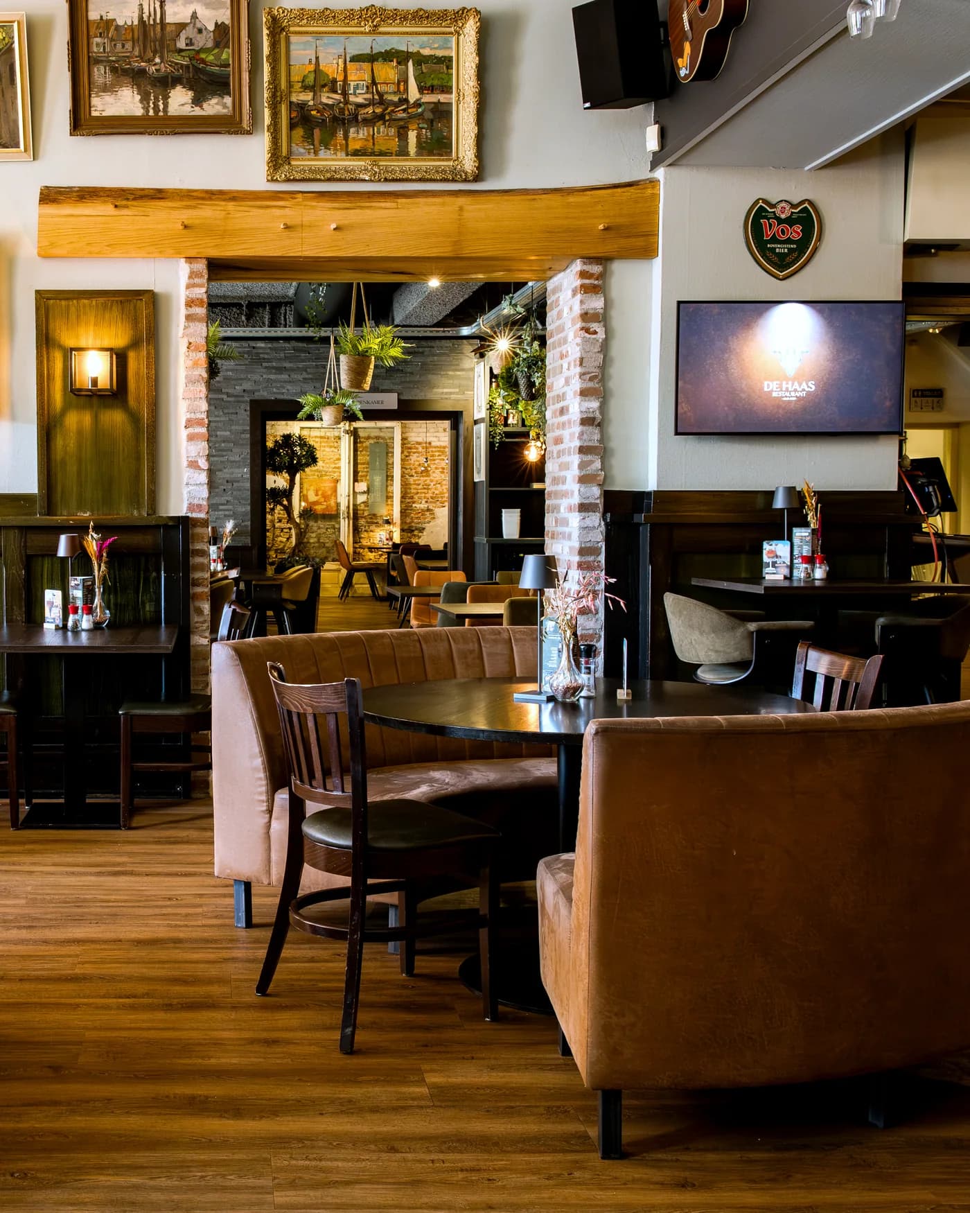 Sfeervolle hoekjes met ronde leren banken, houten tafels en schilderijen aan de muur in Restaurant De Haas Elburg