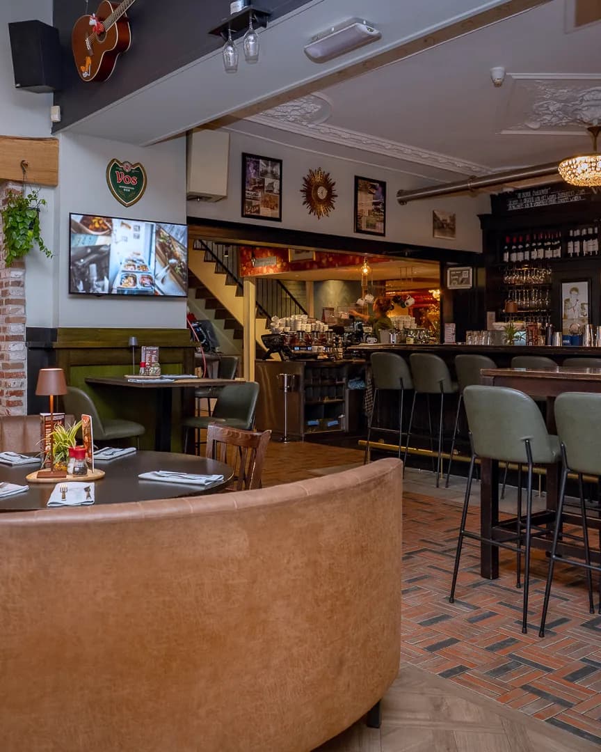 Ronde leren bank met grote tafel en de bar met krukken in Restaurant De Haas Elburg